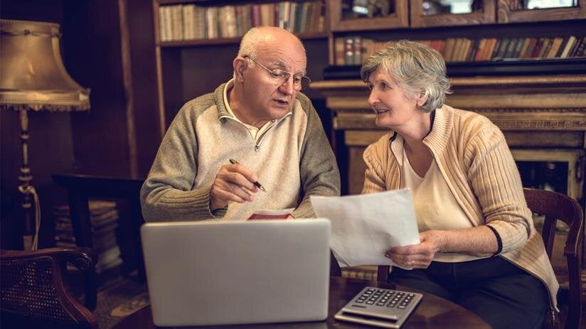 Couple discusses papers at a table, surrounded by books and a laptop, enjoying time together.