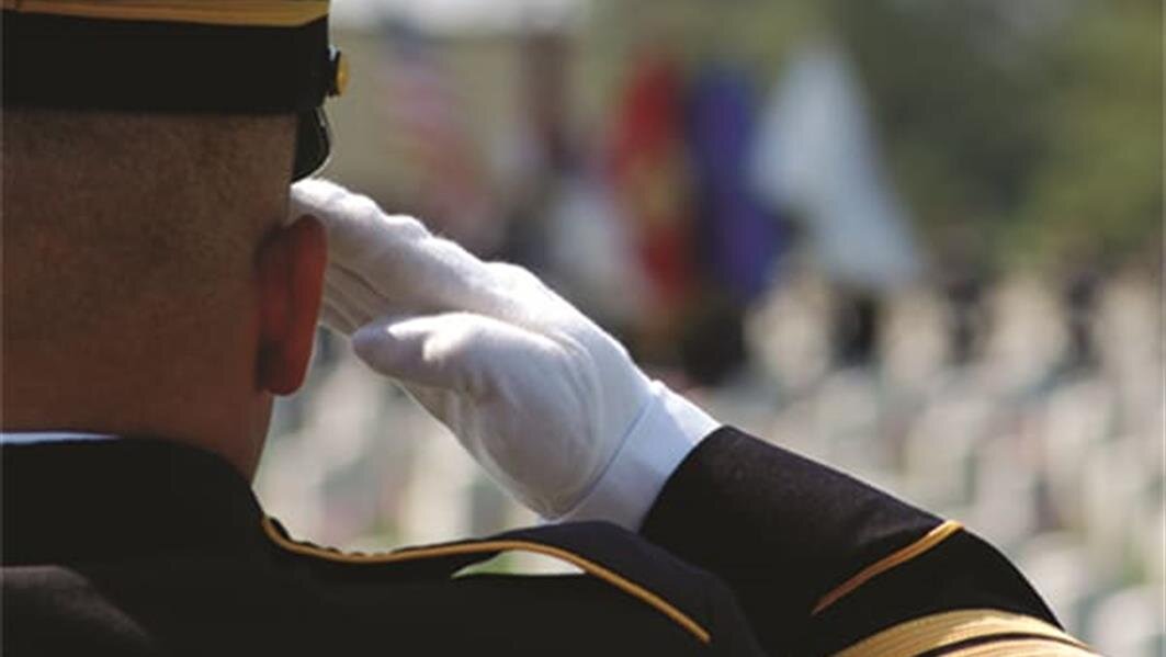 A soldier salutes at a cemetery event honoring fallen heroes and veterans.