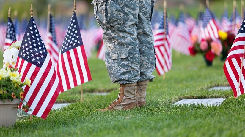 A soldier stands quietly in a cemetery surrounded by flags to honor those who served.
