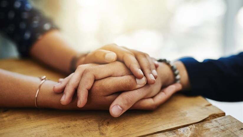 Two hands gently clasped on a wooden table, symbolizing connection and intimacy.