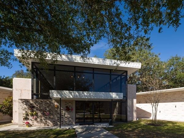 A contemporary building with expansive glass walls surrounded by lush greenery under a clear sky.
