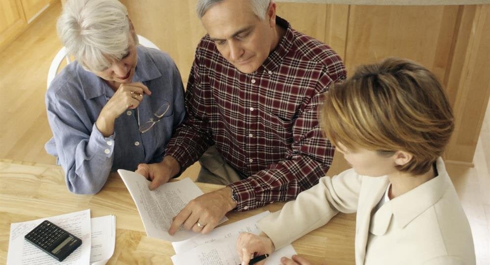 Golden sunlight filters through trees in an autumn park, highlighting vibrant leaves on the ground.