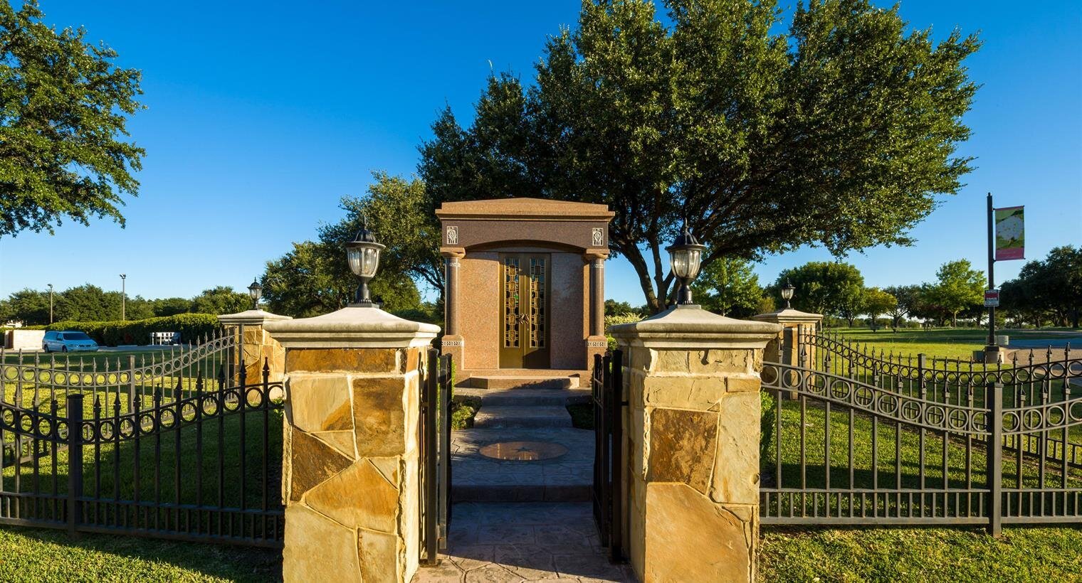 A charming entrance leads into a tranquil park with beautiful trees and clear blue skies.