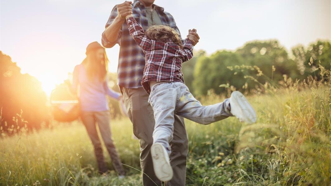 A child plays joyfully in a grassy field while an adult interacts with them.