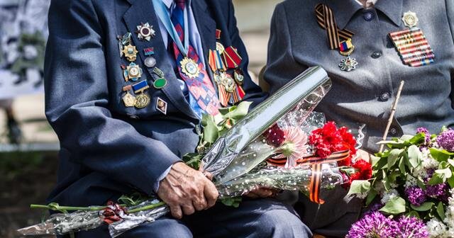 Two veterans display their medals and hold colorful flowers while sharing stories in a park.