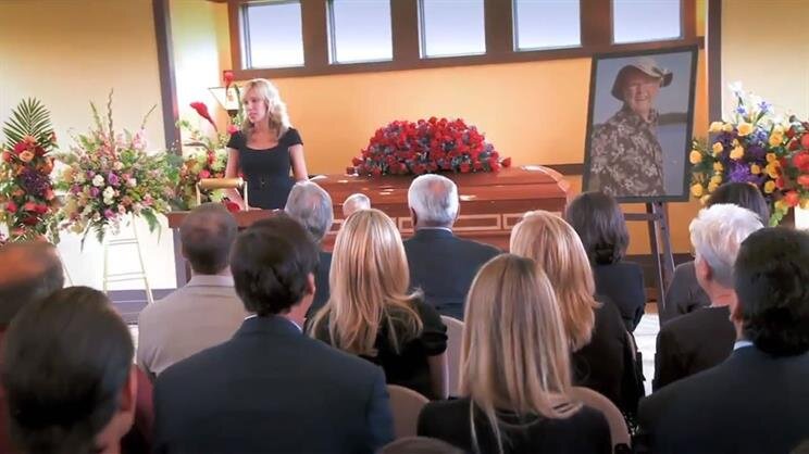 People are standing together in a room for a memorial service with flowers and a portrait.