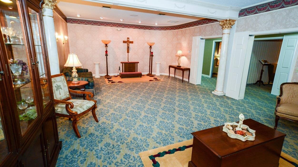 The living room shows furniture like chairs, tables, and lamps arranged in a bright space.