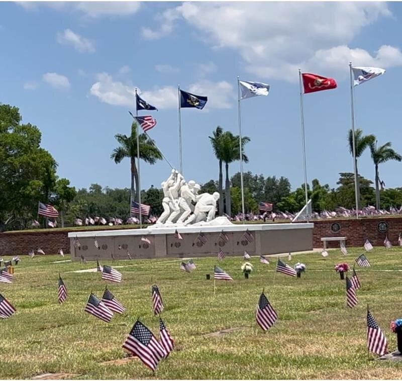 Flags surround a memorial statue as visitors pay respects on a clear day in the park.