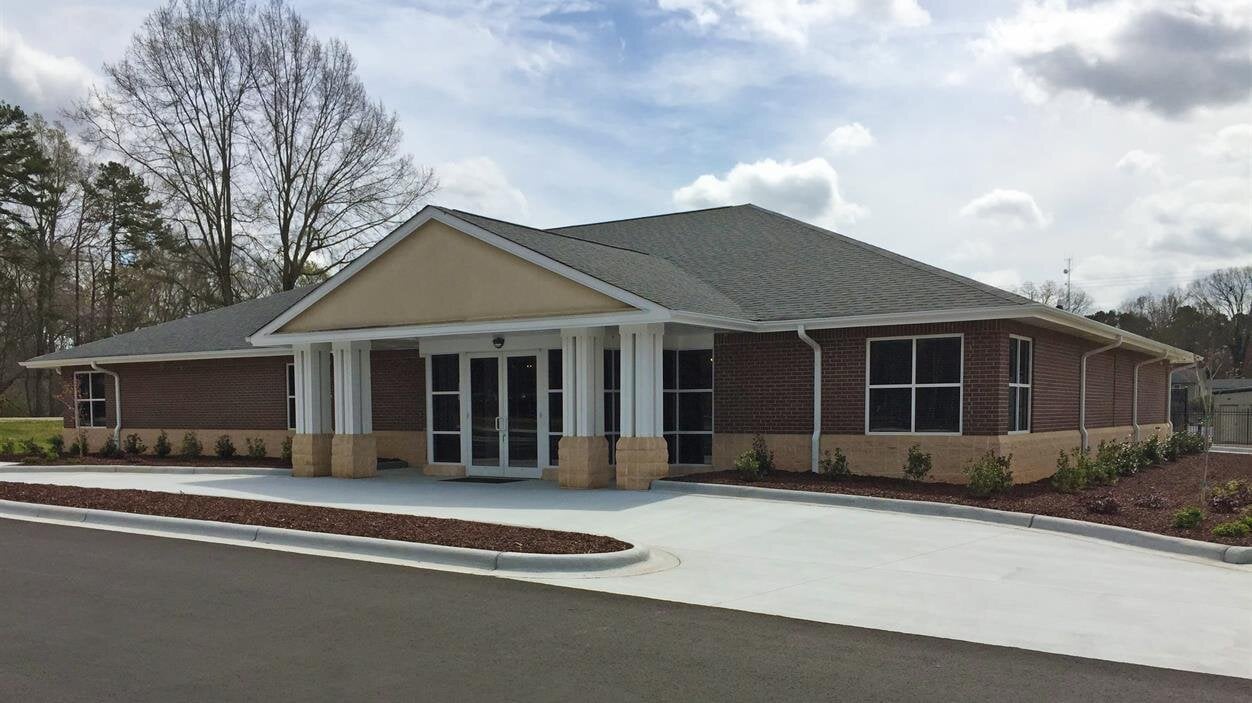 A new building stands with an unfinished exterior on a sunny day in a suburban area.