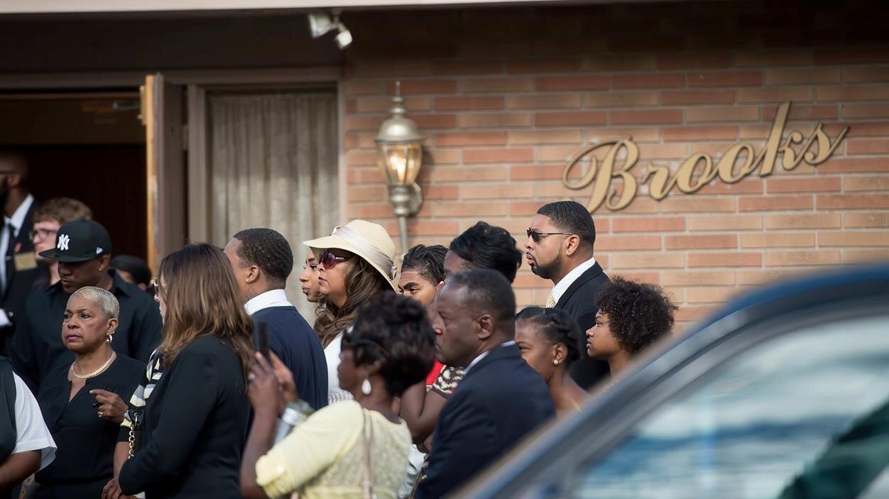 People stand together near a venue with a sign, waiting for an event to begin in the evening.