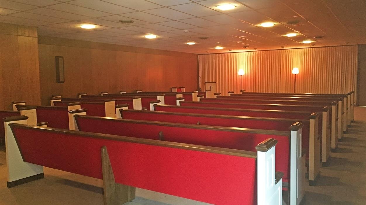 Rows of seats fill a waiting room, lit softly by lights, with a few people sitting quietly.