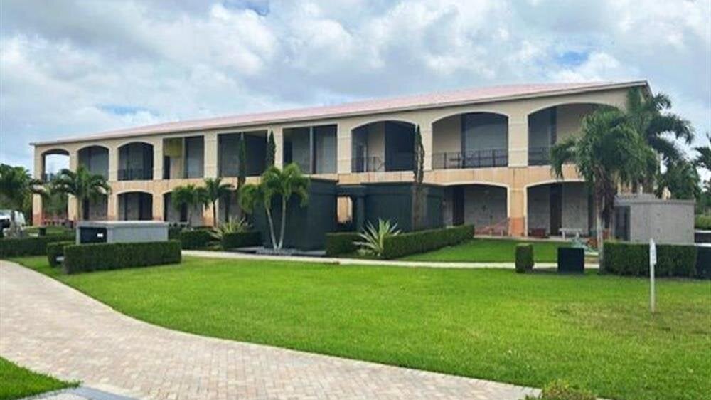 A multi-story building features well-maintained lawns and palm trees on a sunny day.