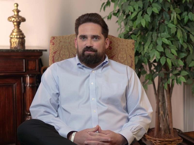 Golden sunlight filters through trees in an autumn park, highlighting vibrant leaves on the ground.