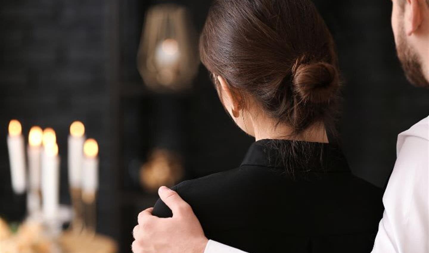 A couple stands together in a warm moment, surrounded by candles and soft light during an event.