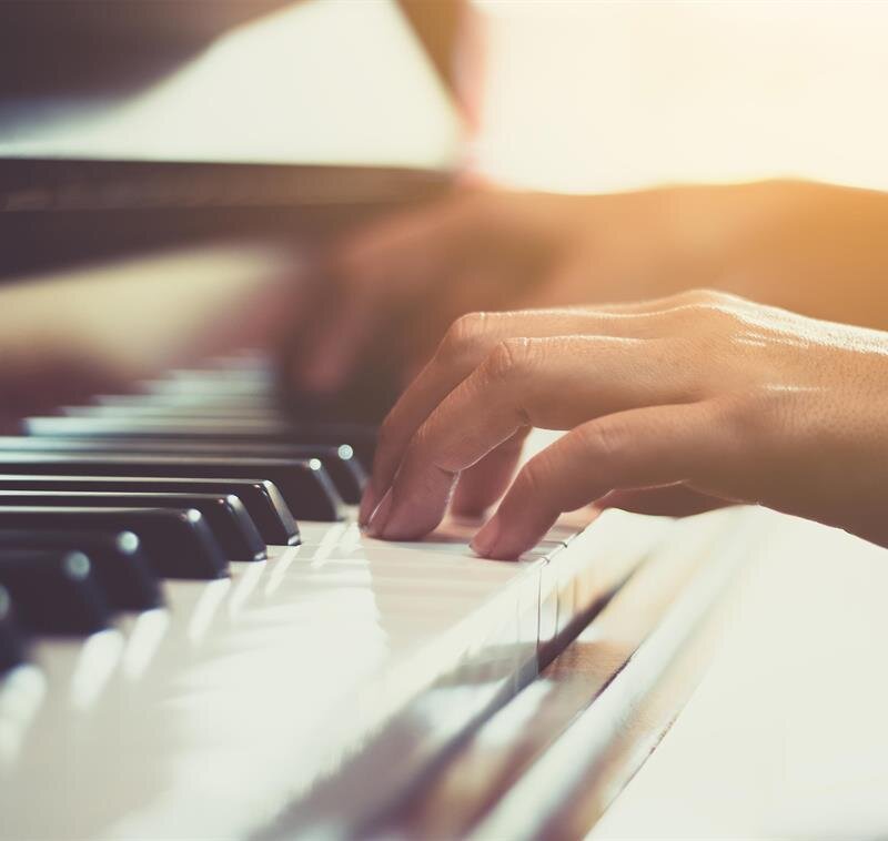 Fingers press down on piano keys as soft music fills the room during a sunny afternoon.
