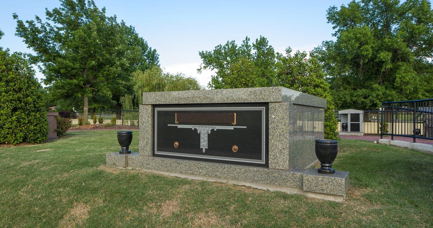 A granite monument featuring a firearm design stands among green trees in a tranquil park.