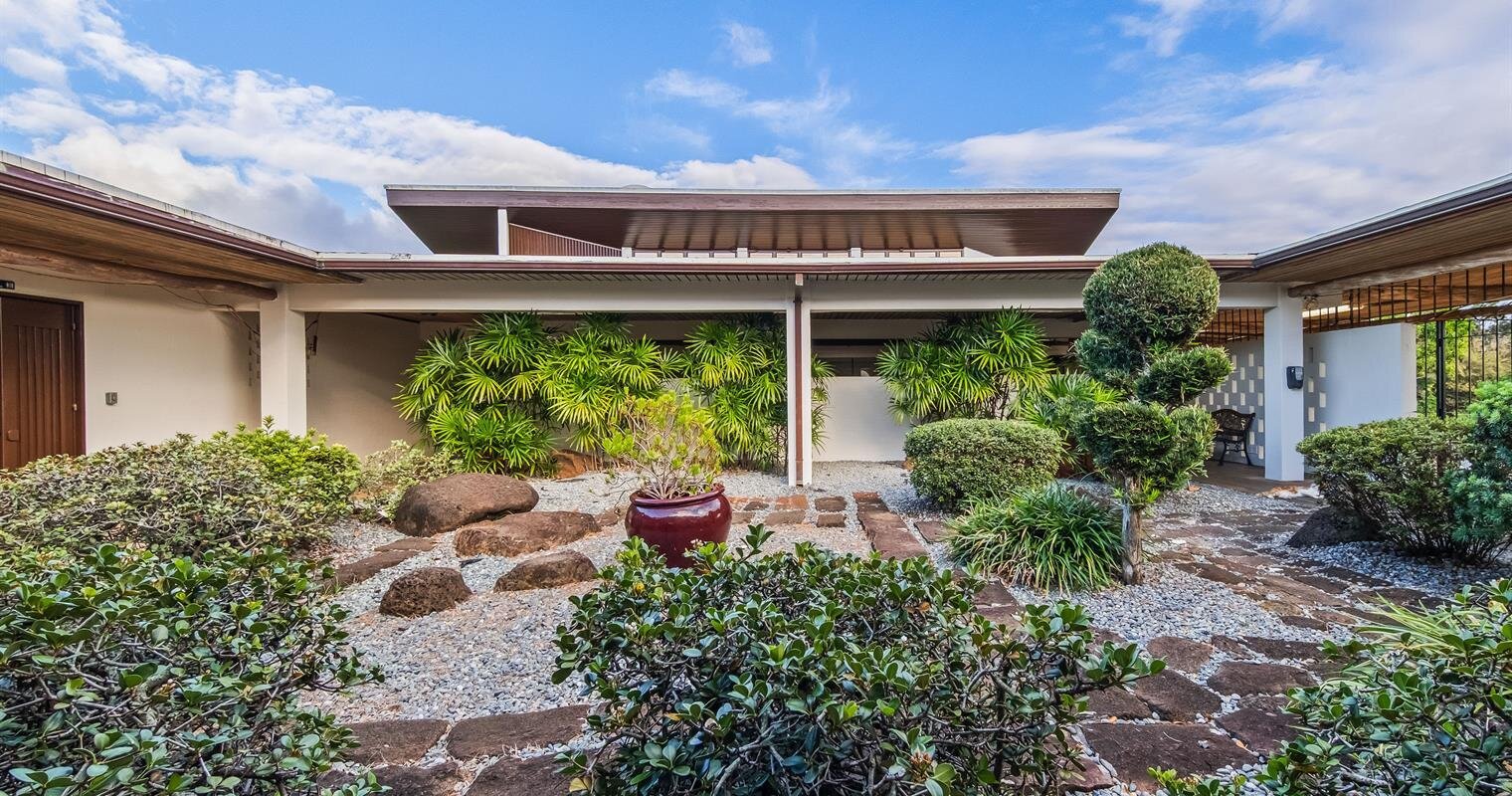 A serene outdoor space showcases lush greenery and carefully arranged stones under a clear blue sky.