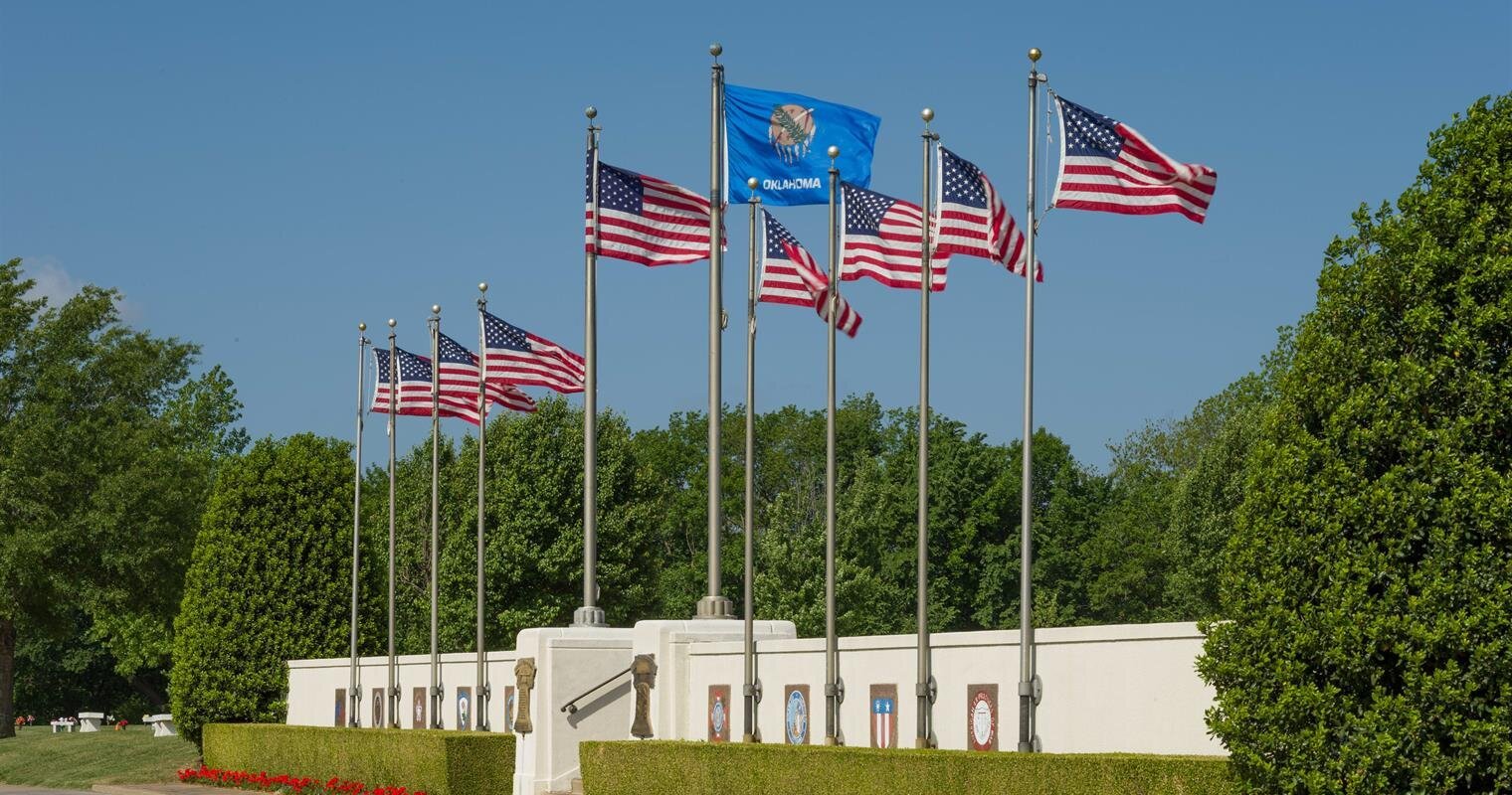 Multiple flags stand tall in front of an attractive building surrounded by greenery.
