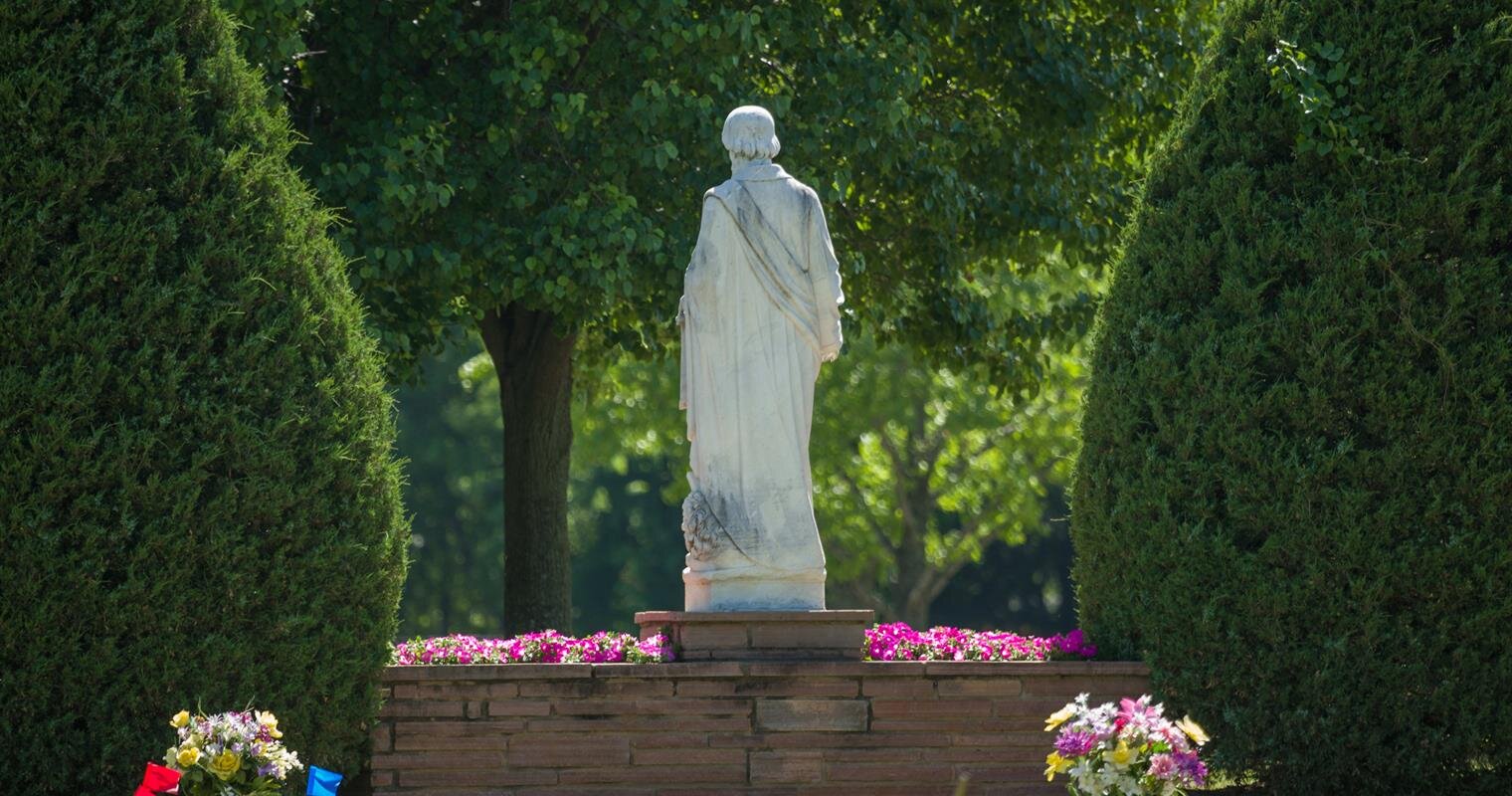 A serene garden features a statue amidst neatly trimmed hedges and colorful flowers in bloom.