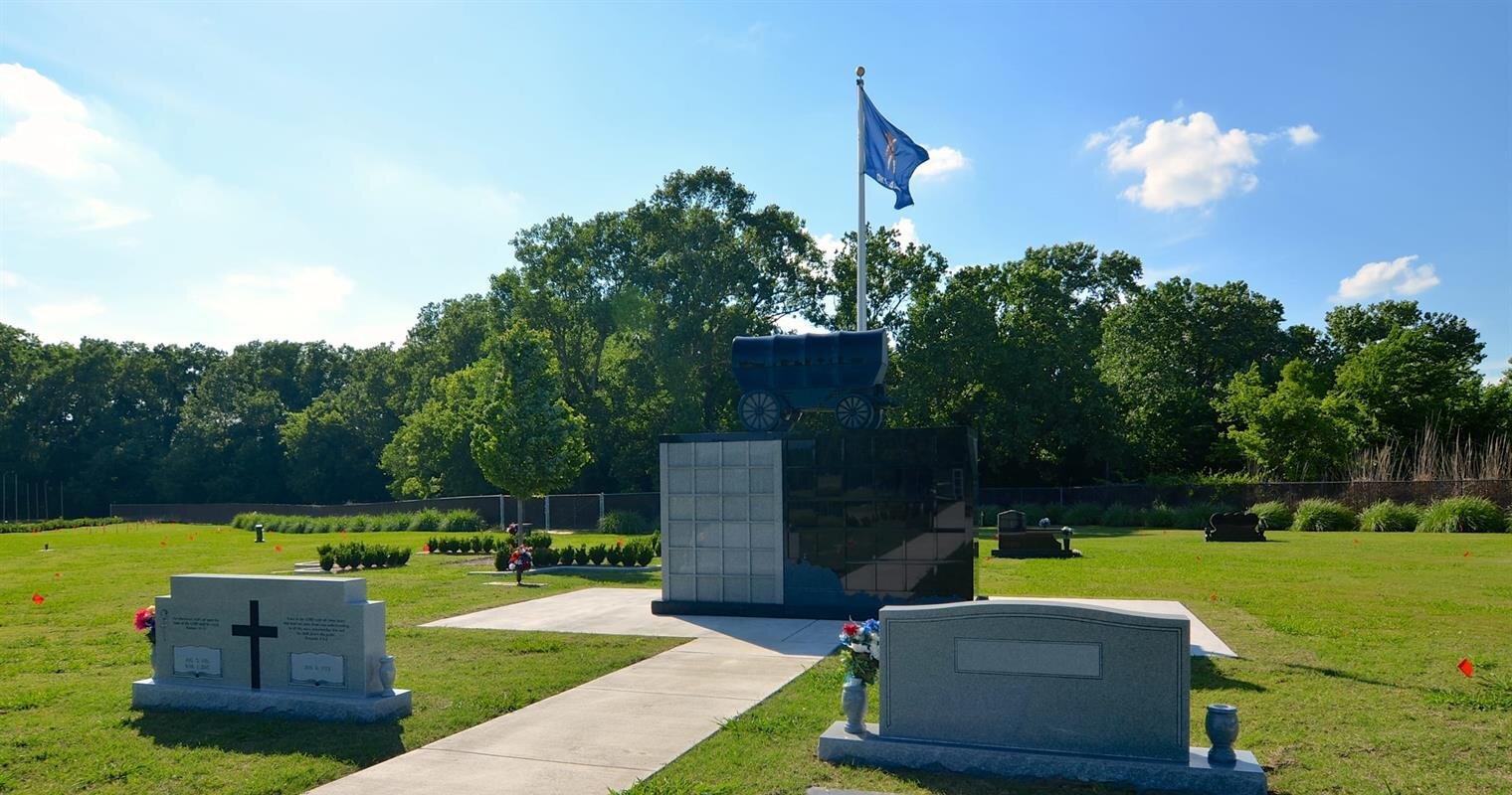 A tranquil memorial area with gravestones, a flag, and well-maintained greenery on a sunny day.