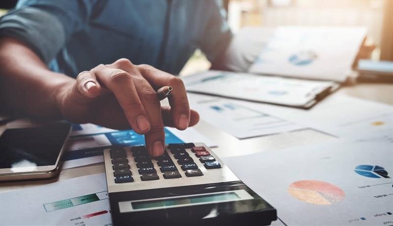 Individual calculates expenses and reviews financial notes on a cluttered desk during the day.