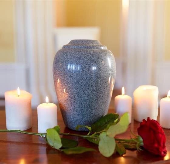A gray urn on a wooden table is surrounded by candles and a red rose, creating peace.