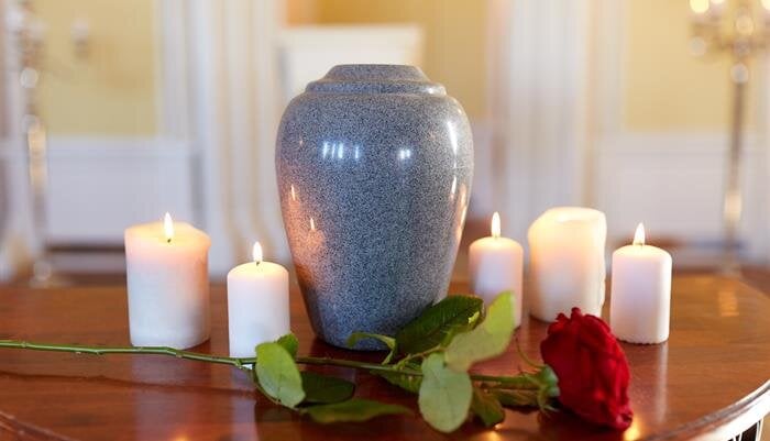 A gray urn on a wooden table is surrounded by candles and a red rose, creating peace.
