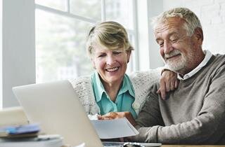 Senior couple smiling as they share a joyful moment browsing on a laptop at home.