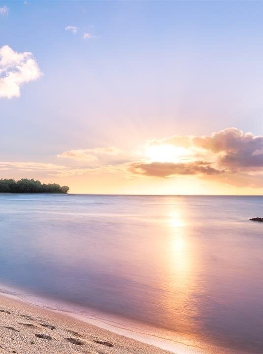 Sunset creates a stunning reflection on the water near a serene beach and lush mountains.