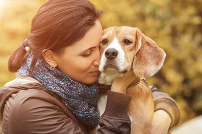 A woman shows affection to her dog while sitting in a park on a sunny day.