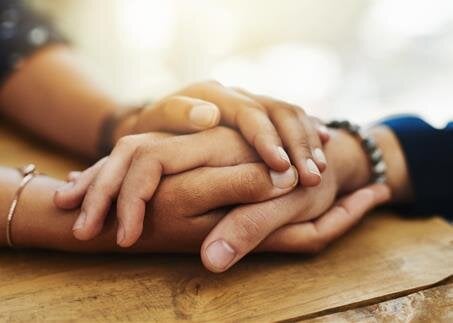 Two hands gently clasped on a wooden table, symbolizing connection and intimacy.
