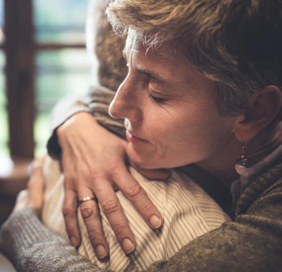 Two people are experiencing a heartfelt hug inside a warm, tranquil space.
