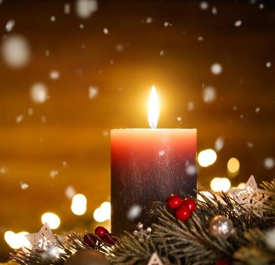 A dark candle shines brightly among holiday decorations as snow gently falls outside.