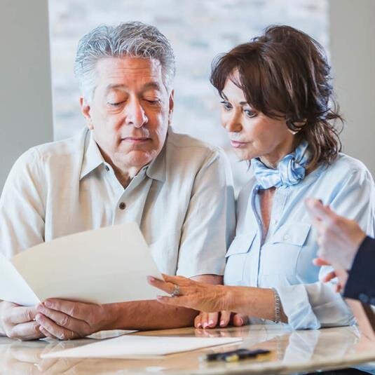 Three individuals sit at a table, discussing and looking at a menu together in a lively cafe.