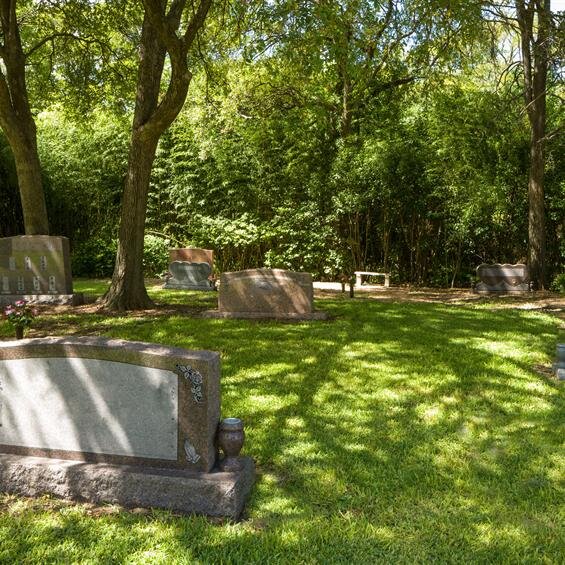 Graves in a tranquil cemetery are shaded by trees, creating a peaceful resting environment.