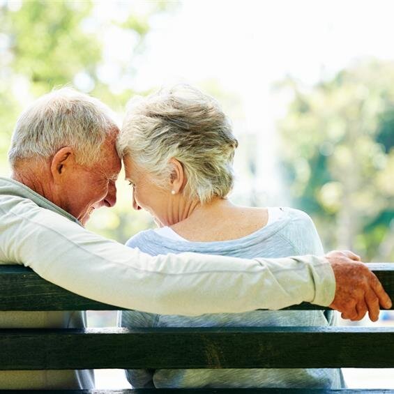 Elderly couple sharing a warm, happy moment together on a bench.