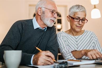Elderly couple sits at a table and writes notes while enjoying their time together indoors.