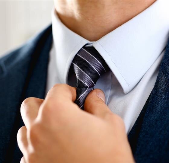 A man in a suit focuses on adjusting his tie, preparing for a professional setting.