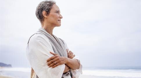 Individual looks thoughtfully towards the ocean, standing on the beach at dawn.