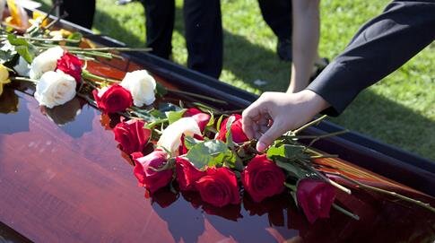Friends and family gather around a casket, placing red and white roses in a farewell gesture.