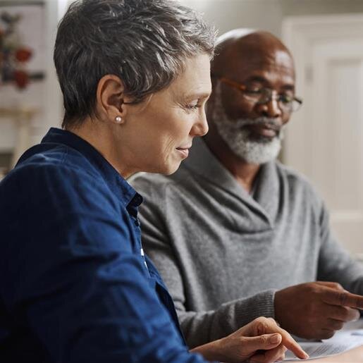 Two elderly individuals share insights and review important papers together at a desk.