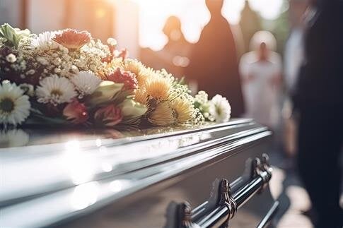 People stand around a casket covered with flowers as they pay their respects during a funeral.