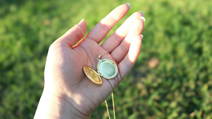 Hand displays various coins and pieces of jewelry under sunlight on green grass.