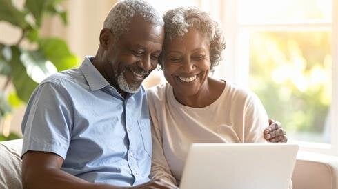 A couple sits on a couch and shares a moment while looking at a laptop.