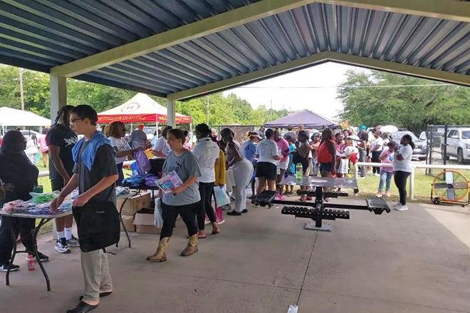 Students and parents line up under a covered pavilion to receive school supplies during the 5th Annual Hurtsboro & Russell County Back to School Drive.