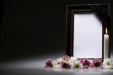 A candle stands next to a blank picture frame with flowers arranged around it.
