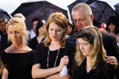 People stand together, showing sadness and support at a funeral while holding umbrellas.