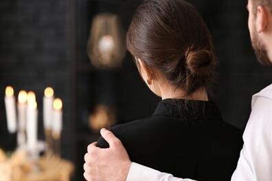 A couple stands side by side in a dimly lit room while candles burn softly on the table.