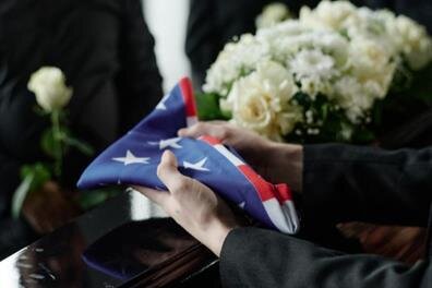 A person holds a folded flag amidst flowers during a memorial service, honoring a hero.