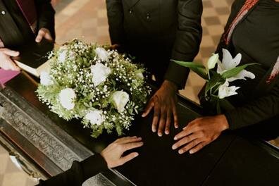 People stand together to honor a loved one at a funeral service with flowers and a casket.